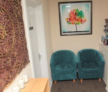 The Uxbridge consulting room — two teal tub chairs beneath a colourful tree canvas, with a carved mandala panel and Welcome candles.