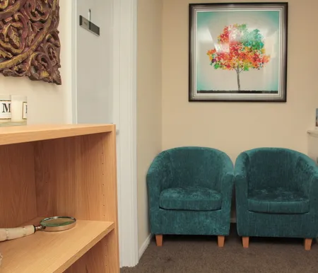 Twin teal tub chairs and a light-wood bookshelf in the Uxbridge consulting room.